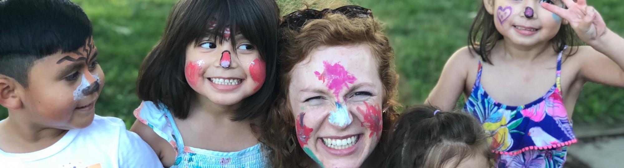 Smiling children and young woman wearing colorful face paint